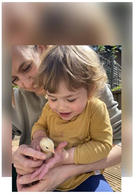 Child holding a small chick while teacher looks on